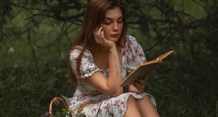 a fair skinned white woman reading a book near trees.jpg.optimal