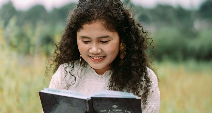 a fair skinned woman of color reading a book in a field.jpg.optimal